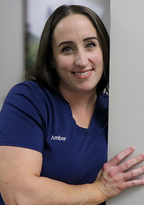 Front Office team member Amber leaning against a hallway wall in a blue top