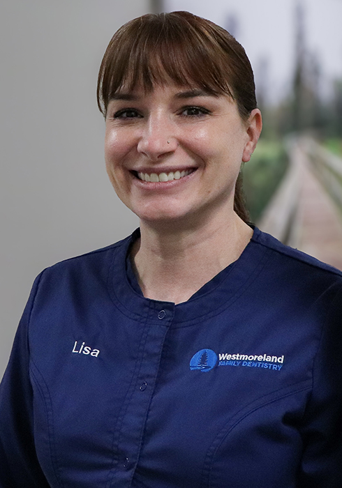 Dental Hygienist Lisa leaning against a hallway wall in blue scrubs