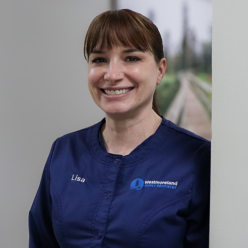 Dental Hygienist Lisa leaning against a hallway wall in blue scrubs