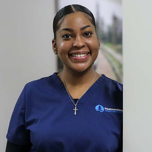 Dental Hygienist Mya leaning against a hallway wall in blue scrubs